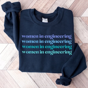 May include: A navy blue sweatshirt with the text "women in engineering" repeated four times in a gradient of purple, blue, and green.