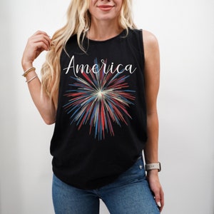 May include: Black sleeveless tank top with a white "America" text and a red, white, and blue firework graphic.