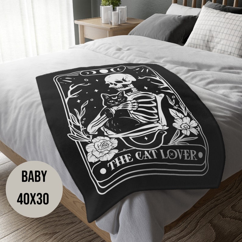 May include: Black and white throw blanket with a skeleton holding a black cat. The blanket features the text "The Cat Lover" in a decorative font.
