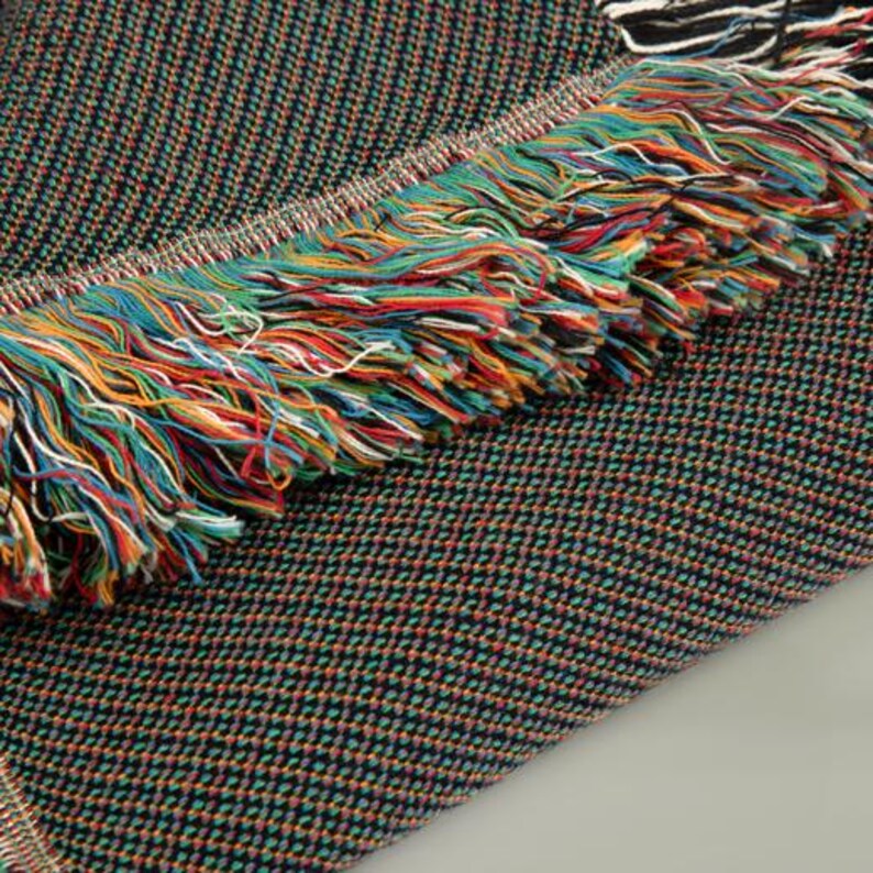 May include: A black woven throw blanket with a colorful fringe. The blanket has a subtle pattern of small, colorful dots.