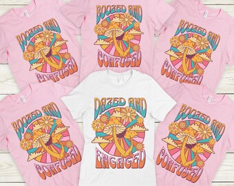May include: Pink and white t-shirts with a retro graphic design featuring mushrooms, flowers, and the phrases "Boozed and Confused" and "Dazed and Engaged". The design has a colourful, psychedelic style.