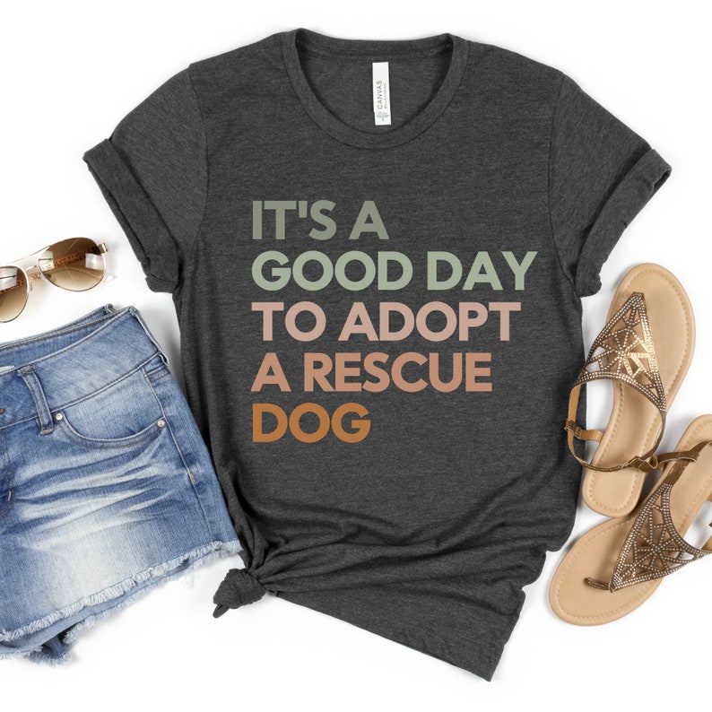 May include: A dark gray t-shirt with the text "It's a good day to adopt a rescue dog" in colorful letters. The text is in a gradient of green, orange, and pink.