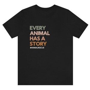 May include: Black t-shirt with the text "EVERY ANIMAL HAS A STORY" in green, tan, and orange. The hashtag "#ANIMALRESCUE" is below the text. The shirt is made of a soft material.