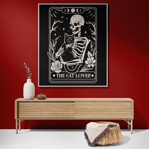 Puede incluir: Ilustraci&oacute;n en blanco y negro de un esqueleto sosteniendo un gato negro. La imagen est&aacute; enmarcada en un borde negro con el texto "The Cat Lover" en la parte inferior.