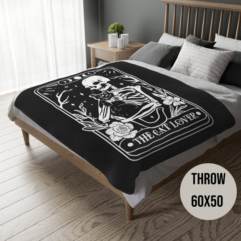 May include: Black and white throw blanket featuring a skeleton holding a cat with the text "The Cat Lover". The blanket is 60 inches by 50 inches.