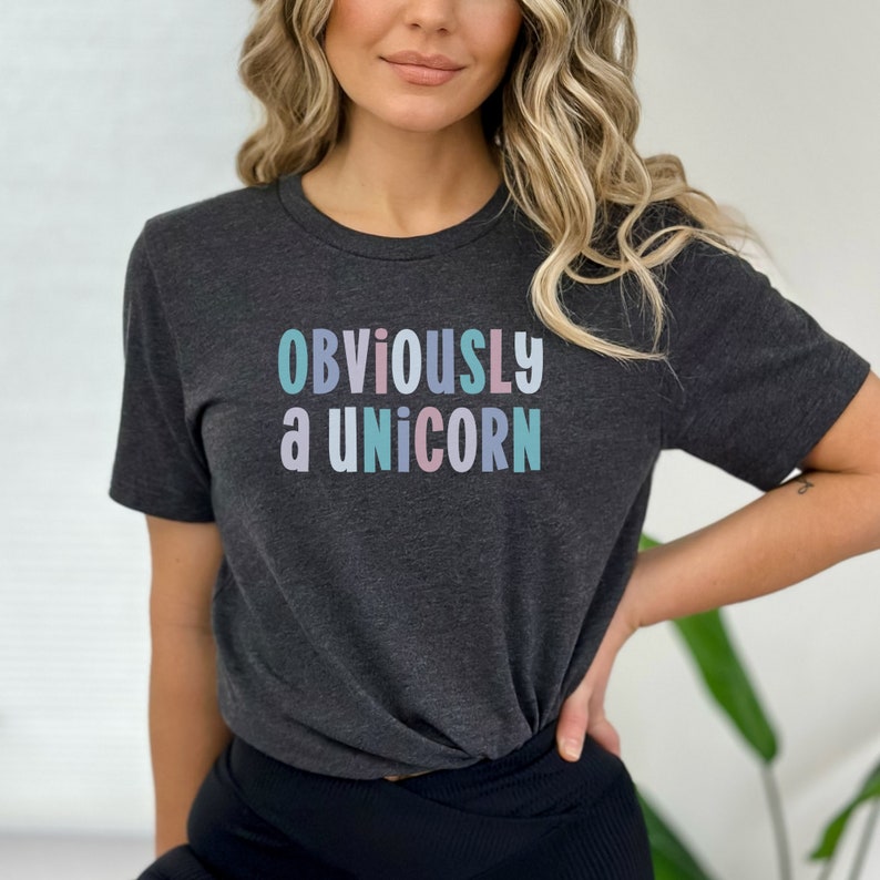 Op de afbeelding: Een donkergrijs T-shirt met de tekst "OBVIOUSLY a UNICORN" in pastelkleuren.