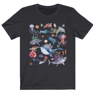 May include: A black t-shirt with a colorful watercolor design of various sea creatures, including a whale, a shark, a jellyfish, a sea turtle, and a starfish.