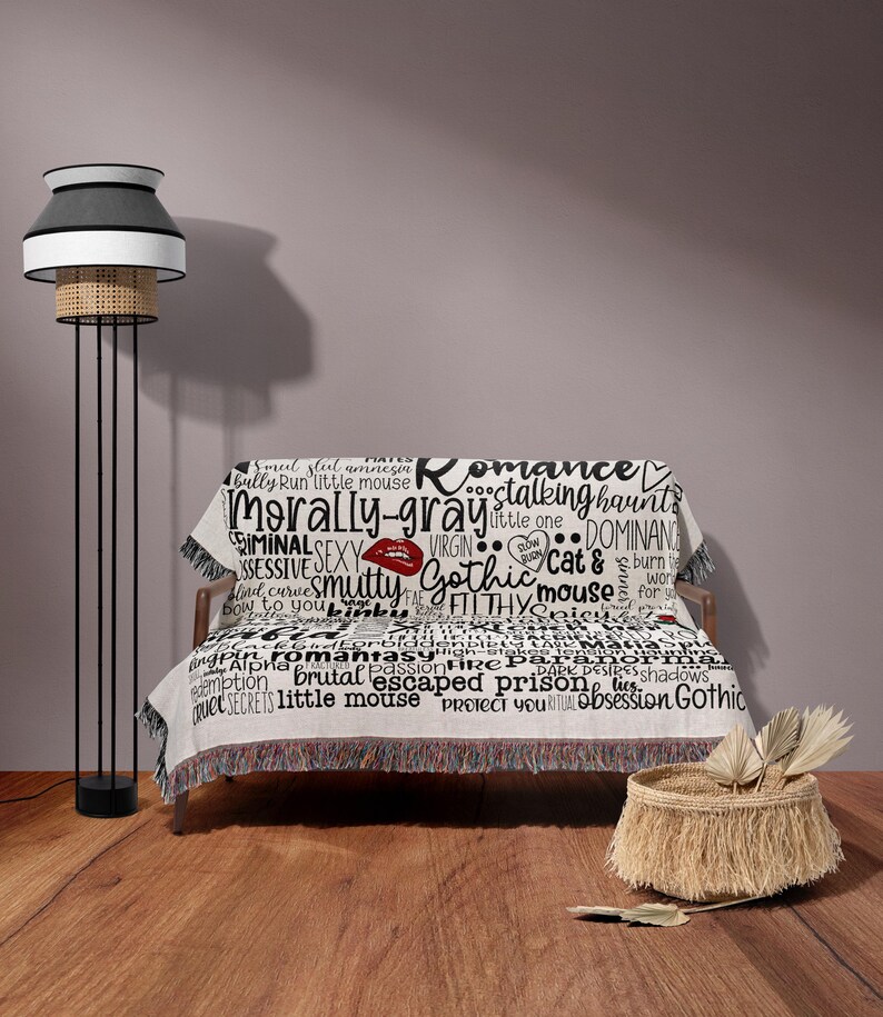 May include: A white throw blanket with black text and a red lip print. The text includes words like "romance", "morally gray", "gothic", "stalking haunts", "dominance", "cat &", "filthy", "little mouse", "escaped prison", "obsession", and "secrets".