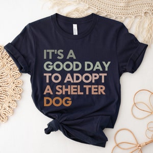 May include: Navy blue t-shirt with the text "It's a good day to adopt a shelter dog" in a multi-colored font.