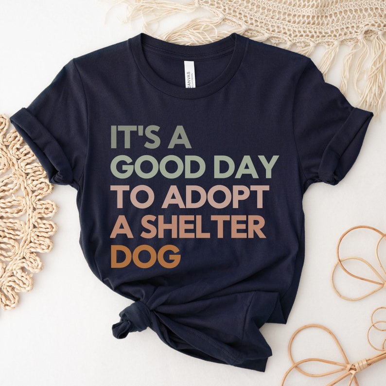 May include: Navy blue t-shirt with the text "It's a good day to adopt a shelter dog" in a multi-colored font.