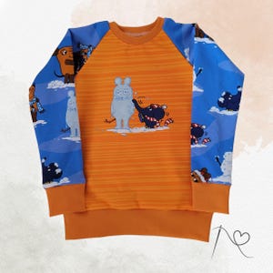Könnte beinhalten: Orangefarbenes Langarm-Sweatshirt mit blauen Ärmeln. Die Ärmel zeigen eine Winterszene mit Zeichentieren. Die Vorderseite hat ein horizontales Streifenmuster und eine Grafik eines Kaninchens und eines Elefanten, die im Schnee spielen. Der Ausschnitt und die Bündchen sind orange.
