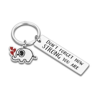 May include: Silver keychain with a rectangular tag that reads "DON'T FORGET HOW STRONG YOU ARE." It includes a charm of a white elephant with red hearts. The keychain is a thoughtful gift.