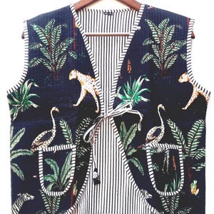 May include: A quilted vest with a dark blue jungle print featuring leopards, birds, and palm trees. The vest has a striped white and black interior and a tie closure. The vest has two pockets.