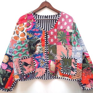 Könnte beinhalten: Patchwork-Jacke mit bunten Blumen-, Tier- und geometrischen Mustern in Pink, Blau, Grün und Orange. Die Jacke hat ein schwarz-weiß gestreiftes Futter und einen Besatz sowie zwei Vordertaschen.