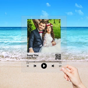 May include: A digital music player interface with a photo of a couple in a wedding setting. The interface shows the song title, artist name, play controls, and a timer. The background is a beach scene.