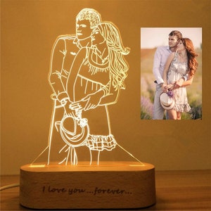 May include: A wooden base with a light-up acrylic panel featuring a line drawing of a couple embracing. The base has the text "I love you...forever..." engraved on it. A photo of a couple is visible in the background.
