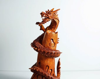 May include: A wooden sculpture of a dragon wrapped around a pillar. The dragon is carved in detail and has a fierce expression. The sculpture is made of a reddish-brown wood.