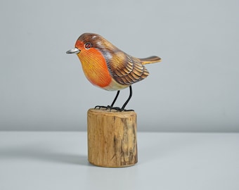 Pode incluir: Estatueta de pisco-de-peito-ruivo em madeira pintada à mão, com cabeça castanha, peito laranja e detalhes nas penas das asas. A ave está pousada num pequeno bloco de madeira natural, um objeto decorativo encantador.