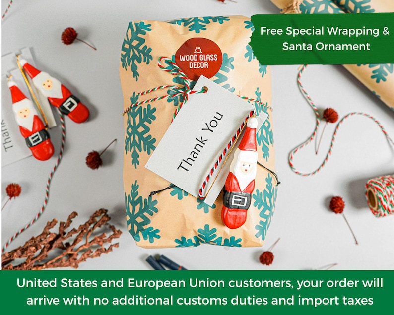 May include: A rectangular package wrapped in tan paper with a teal snowflake pattern, tied with red and white twine. A circular red Wood Glass Decor sticker, a white Thank You tag, and a small wooden Santa Claus ornament are attached.