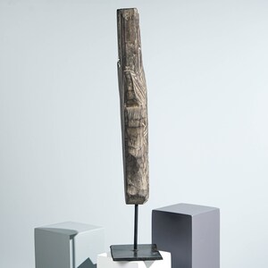 May include: A carved wooden sculpture with intricate details, mounted on a black metal stand. The sculpture is dark brown and has a rustic appearance.
