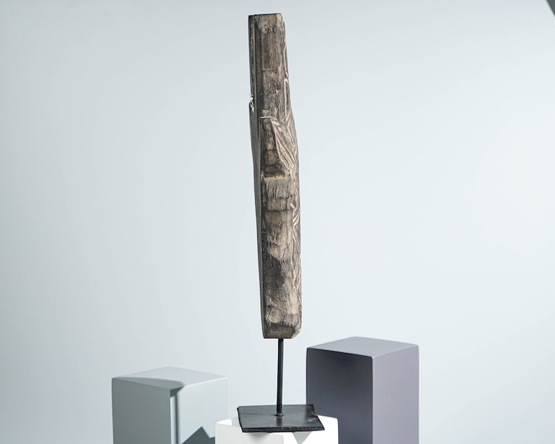 May include: A carved wooden sculpture with intricate details, mounted on a black metal stand. The sculpture is dark brown and has a rustic appearance.