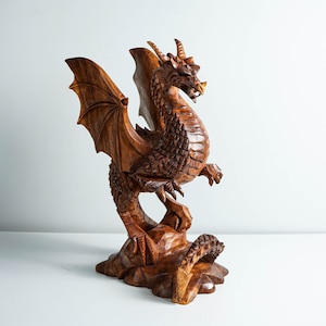 May include: A hand-carved wooden dragon sculpture with intricate details. The dragon is depicted with outstretched wings, a long tail, and a fierce expression. The sculpture is made of dark brown wood and has a natural finish.