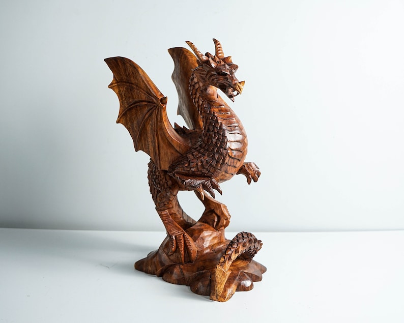 May include: A hand-carved wooden dragon sculpture with intricate details. The dragon is depicted with outstretched wings, a long tail, and a fierce expression. The sculpture is made of dark brown wood and has a natural finish.