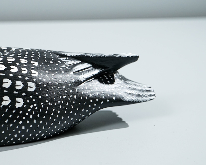 May include: A carved wooden bird figurine featuring a black body with white painted spots and markings. The tail section shows detailed carved feather textures with white highlights along the edges, contrasting against the dark black base color.