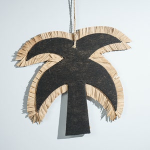 May include: A black palm tree cutout with a fringed raffia border. The palm tree is hanging from a string.