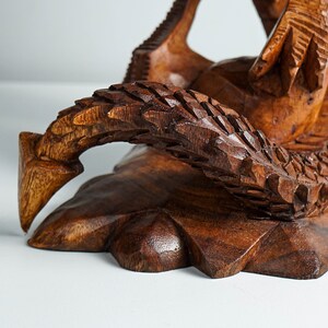 May include: A wooden sculpture of a dragon with intricate details. The dragon is carved in a dark brown color and has a textured surface. The dragon's tail is curled around its body, and its head is raised up.