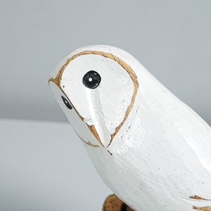 K&ouml;nnte beinhalten: Eine wei&szlig;e Holz-Eulenfigur mit schwarzen Augen und hellbraunen Konturen. Die Eule ist wei&szlig; lackiert und hat ein antikes Finish, das ihr ein rustikales Aussehen verleiht. Der Kopf der Eule ist leicht nach links gedreht.