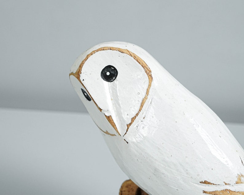 K&ouml;nnte beinhalten: Eine wei&szlig;e Holz-Eulenfigur mit schwarzen Augen und hellbraunen Konturen. Die Eule ist wei&szlig; lackiert und hat ein antikes Finish, das ihr ein rustikales Aussehen verleiht. Der Kopf der Eule ist leicht nach links gedreht.