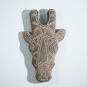 May include: A wooden giraffe head wall decor with a geometric design. The giraffe is carved from dark wood and has a detailed pattern.