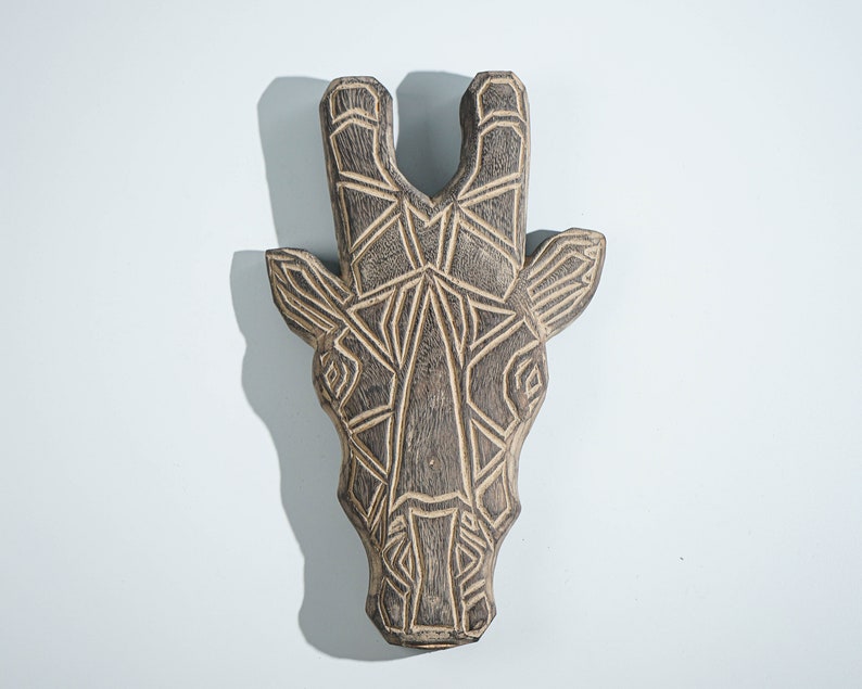 May include: A wooden giraffe head wall decor with a geometric design. The giraffe is carved from dark wood and has a detailed pattern.