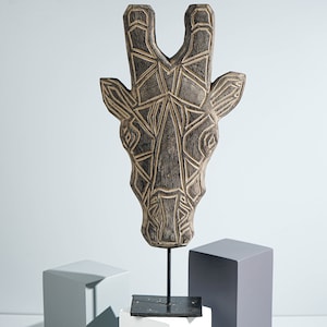May include: A wooden giraffe head sculpture with a geometric design, painted in black and brown, mounted on a black metal stand.