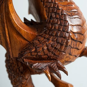 May include: A detailed wooden carving of a dragon with intricate scales and claws. The dragon is in a curled position with its wings spread out.