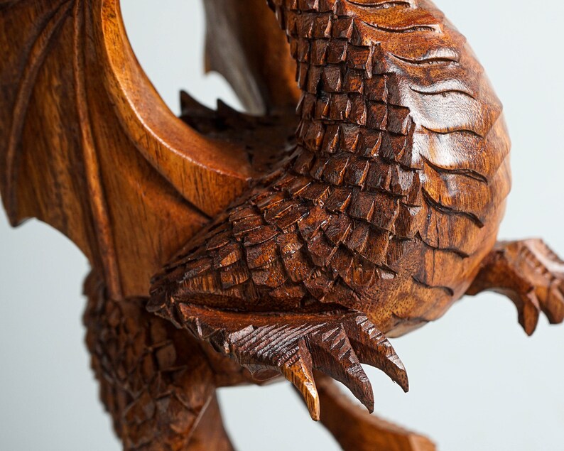 May include: A detailed wooden carving of a dragon with intricate scales and claws. The dragon is in a curled position with its wings spread out.
