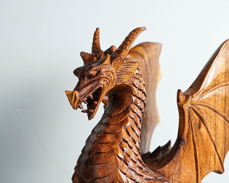 May include: A wooden dragon sculpture with intricate details, featuring a fierce expression and outstretched wings. The dragon is carved from a rich brown wood and has a textured surface.