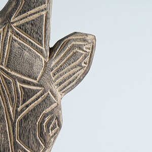May include: Close-up of a wooden animal head sculpture with intricate geometric carvings. The sculpture is painted in shades of brown and black.