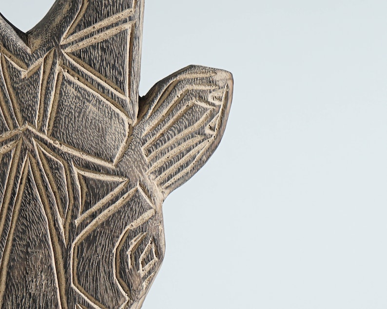 May include: Close-up of a wooden animal head sculpture with intricate geometric carvings. The sculpture is painted in shades of brown and black.
