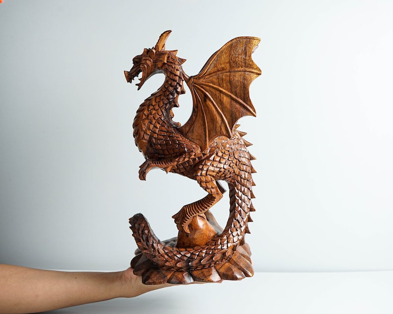 May include: A hand-carved wooden dragon sculpture with intricate details. The dragon is brown and has a long tail, wings, and a fierce expression.