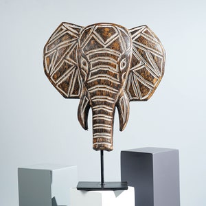 Peut inclure: Sculpture de tête d'éléphant en bois avec un motif géométrique sculpté dans le bois. La sculpture est peinte en brun et blanc et est montée sur un support en métal noir.