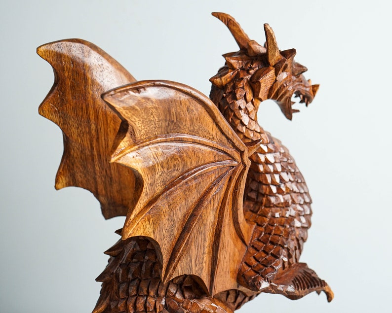 May include: A wooden dragon sculpture with detailed carvings of scales and wings. The dragon is brown and has a fierce expression.