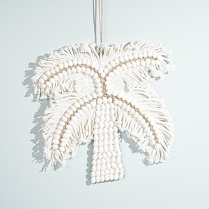 May include: White palm tree wall hanging made of woven rope and white beads. The palm tree has a fringe design and is hanging from a string.