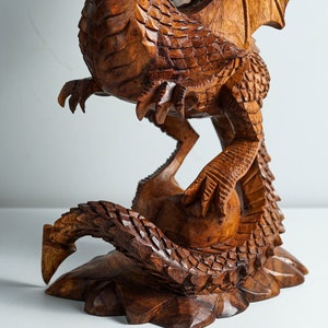 May include: A hand-carved wooden dragon sculpture with intricate details. The dragon is depicted in a coiled position with its wings spread out. The sculpture is made of a rich brown wood and has a natural finish.