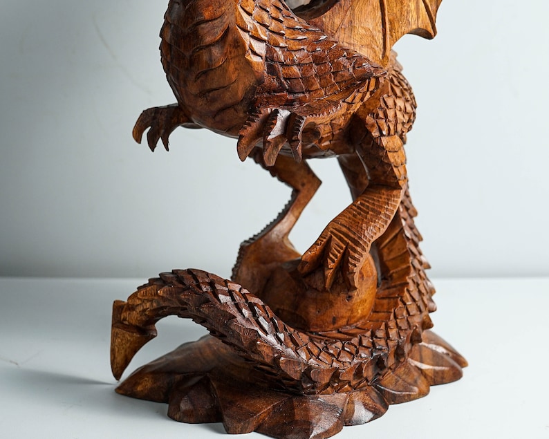 May include: A hand-carved wooden dragon sculpture with intricate details. The dragon is depicted in a coiled position with its wings spread out. The sculpture is made of a rich brown wood and has a natural finish.