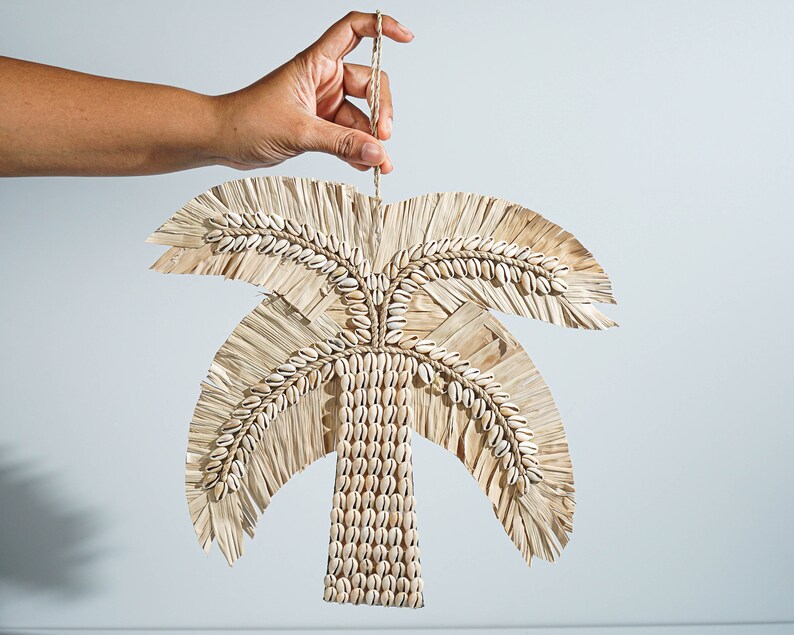 May include: A woven palm tree wall hanging with white seashells. The palm tree is made of natural materials and has a rustic look.