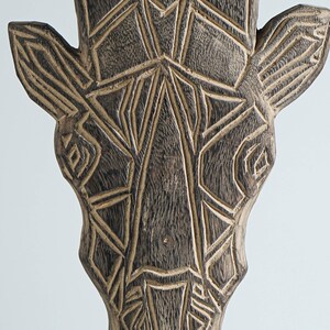May include: A wooden giraffe head sculpture with a geometric pattern carved into the surface. The sculpture is painted in shades of brown and black.