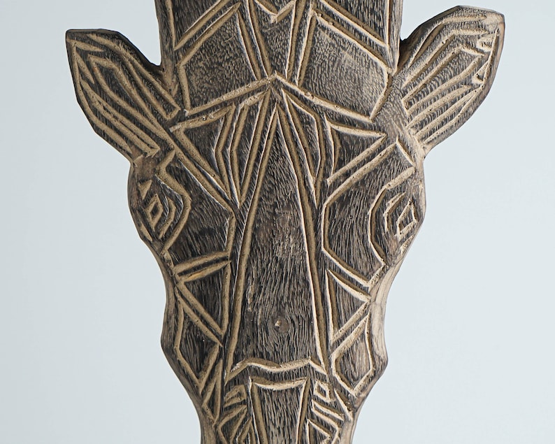 May include: A wooden giraffe head sculpture with a geometric pattern carved into the surface. The sculpture is painted in shades of brown and black.