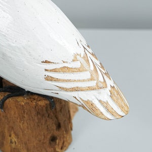 K&ouml;nnte beinhalten: Geschnitzte Holzfigur eines Vogels, wei&szlig; bemalt mit gewischten Details. Der Vogelk&ouml;rper sitzt auf einem kleinen, nat&uuml;rlichen Holzsockel. Die F&uuml;&szlig;e des Vogels sind schwarz. Das Design hat eine rustikale, handwerkliche &Auml;sthetik.